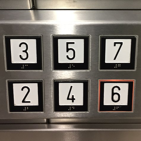 Taster in einem Aufzug: Schwarze Zahlen auf weißem Grund, die außen schwarz umrandet sind. 