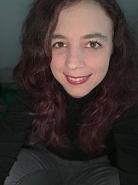 Portrait einer lächelnden Frau mit langen dunkelroten lockigen Haaren.