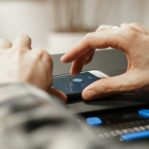 Großaufnahme von einer Hand, die über den Bildschirm eines Smartphones wischt. Davor liegt eine Braille-Zeile. 