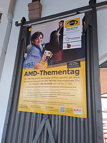An einer Tür hängt ein großes Plakat zum AMD Thementag. Hier sieht man eine ältere Dame, die einen Vortrag besucht. 