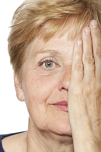 Eine Seniorin mit kurzen Haaren hält sich mit der Hand ein Auge zu