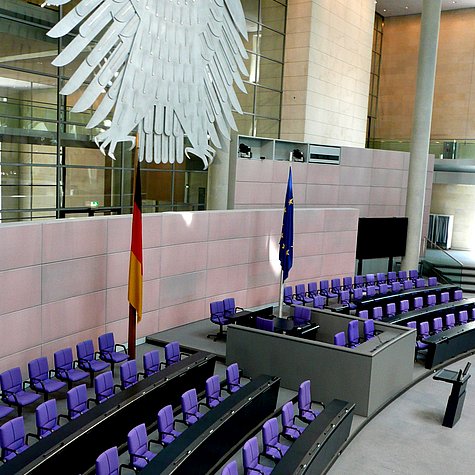 Stuhlreihen im Plenarsaal des Deutschen Bundestages, darüber hängt der Bundesadler.