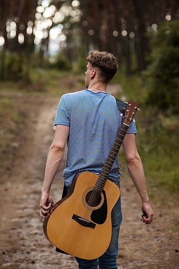 Ein junger Mann geht mit seiner Gitarre durch den Wald.