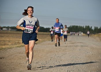 Fröhlich aussehende Läuferin joggt über einen ebenen Sandweg.