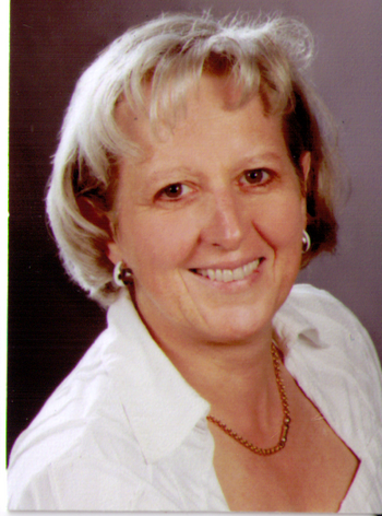 Portrait einer Frau mit kurzem blonden Haar, silbernen Ohrringen und weißer Bluse, lächelt
