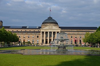 Kurhaus Wiesbaden mit Springbrunnen und Grünanlage im Vordergrund.