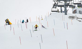Blinder Skifahrer fährt unter Anweisung eines parallel abfahrenden Guides im Slalom Abfahrtski