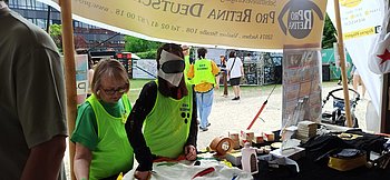 Eine junge Frau mit Simulationsbrille ertastet Alltagsgegenstände in verschiedenen Taschen