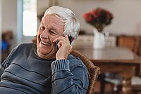 Laughing senior man talking on a cellphone in at home