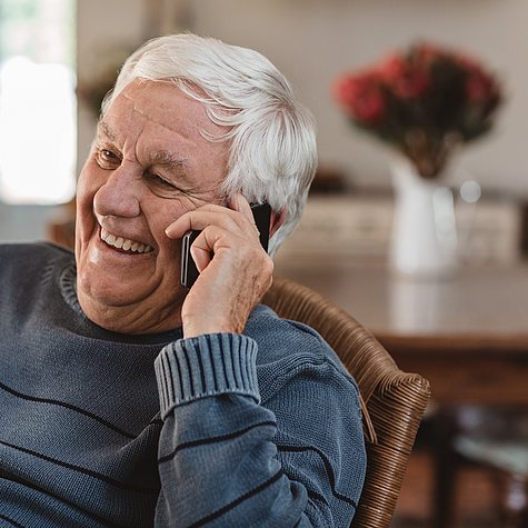Laughing senior man talking on a cellphone in at home