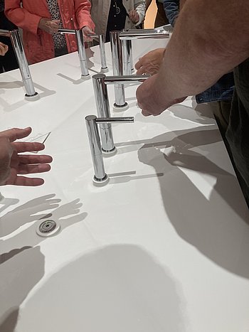 Hände ertasten Hähne eines kunstvoll gestalteten Waschbeckens in Dreiecksform 