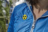 Großaufnahme einer blauebn Jacke, an der ein runder Stecker in gelb mit drei schwarzen Punkten befestigt ist.
