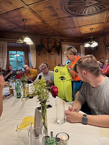 Anne stellt beim Abendessen den Teilnehmern das gemeinsame Gruppenshirt vor. Es ist Neongelb. Vorne ist das Logo der Pro Retina und der Spruch "Don´t try, just Do it!" Auf der Rückseite ist sie Route mit den entsprechenden Höhenmetern bis zum Gipfel aufgezeichnet
