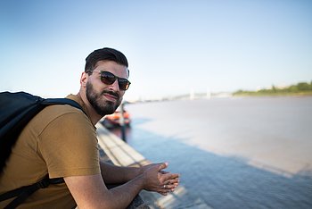 Ein junger Mann mit braunen Haaren und Bart lehnt an einem Geländer.