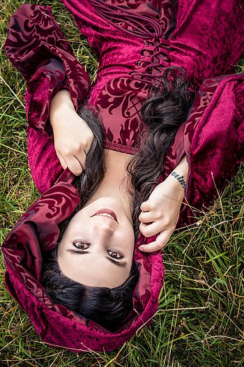 Portrait von Nadine Nadine liegt mit einem weinroten langen Kleid im Gras