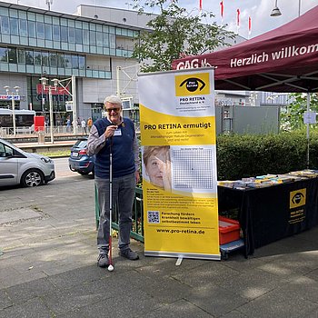 Joachim Schulte steht neben einem PRO RETINA Austeller an einem Stand mit Broschürenauslage 