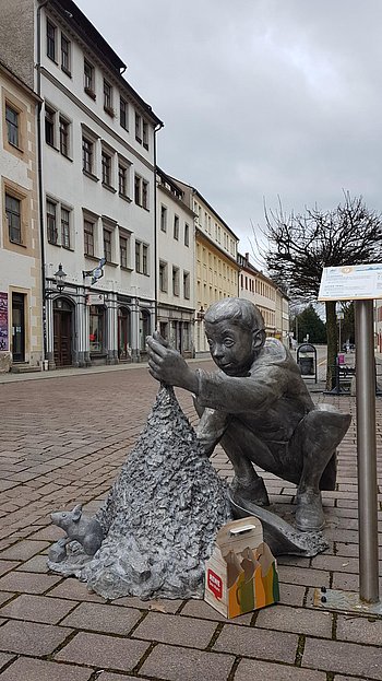 Eine weitere Plastik: ein Junge hockt auf der Straße und baut eine Matschburg
