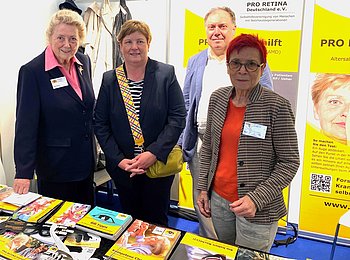 Eine Gruppe von drei Frauen und einem Mann stehen vor PRO RETINA-Roll Ups. Vor ihnen ein Tisch mit PRO RETINA-Broschüren.