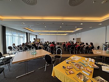 Das Bild zeigt unseren Seminarraum. Im Vordergrund steht ein Tisch mit Infobroschüren der Pro Retina, dahinter Stuhlreihen mit den Seminarteilnehmern.