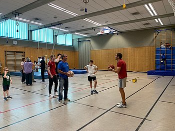 Anleitung für ein Ballspiel am Basketballkorb. Jugendliche und Eltern spielen gemeinsam.