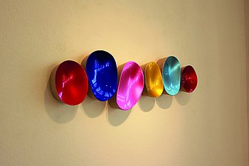 Das Bild zeigt sechs Wandobjekte des Künstlers Willi Siber. Die runden, schalenartigen Objekte sind innenfarbig: rot, blau, pink, gelb, türkis, rot.