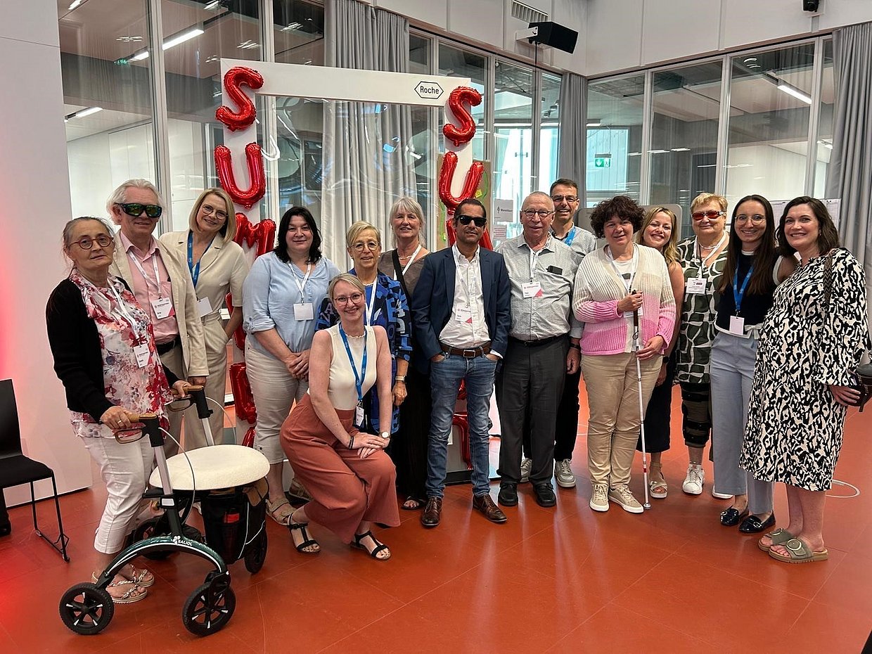 Summer Summit Roche 2025 Eine Gruppe von 15 Menschenin sommerlich-schicker Kleidung steht vor roten Luftballons, die den Schriftzug "Summer Summit" bilden und lächelt in die Kamera