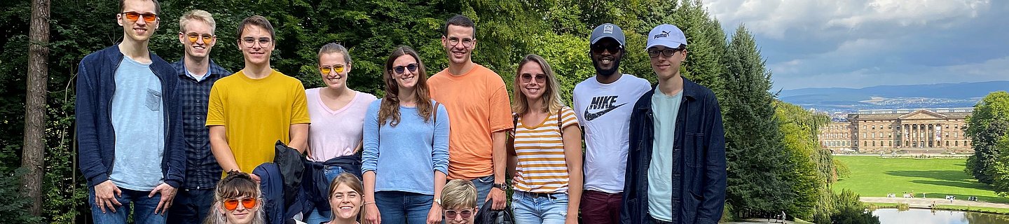 Eine Gruppe junger Menschen, teilweise mit Kantenfilterbrille und Blindenlangstock steht bei gutem Wetter in einem Park. Im Hintergrund sieht man ein Schloss. 