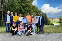 Eine Gruppe junger Menschen, teilweise mit Kantenfilterbrille und Blindenlangstock steht bei gutem Wetter in einem Park. Im Hintergrund sieht man ein Schloss. 
