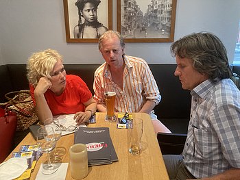 Drei Personen sitzen am Tisch und sind ins Gespräch vertieft