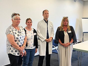 Auf dem Foto sind von links nach rechts  Roswitha Kaarst in einem weißen T-Shirt mit grau-schwarzen Punkten, Nadine Praum (Beraterin in Ausbildung) mit einen weiß-bunten Shirt und einer schwarzen Jacke, Dr. Stanzel in einem weißen Kittel und Marion Palm Stalp in einem weißen Kleid und einer schwarzen Jacke zu sehen.