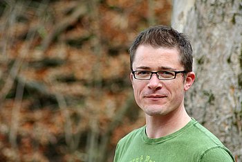 Studienteilnehmer Julian Portraitaufnahme eines jungen Mannes. Er trägt eine Brille und ein grünes Shirt