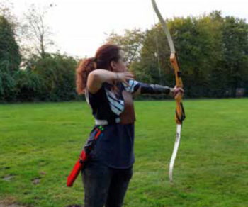 Foto: Eine junge Frau, welche einen Bogen spannt. Sie steht mit dem Rücken zur Kamera