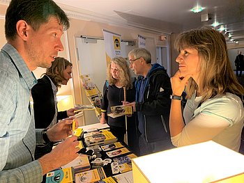 Ein Mann und eine Frau unterhalten sich an einem Infostand von PRO RETINA. Im Hintergrund sind weitere Personen zu sehen.