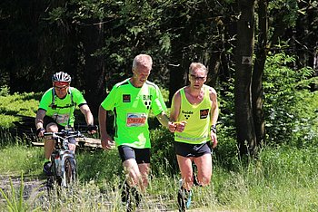 Zwei Tandemläufer und ein Fahrradfahrer im Wald