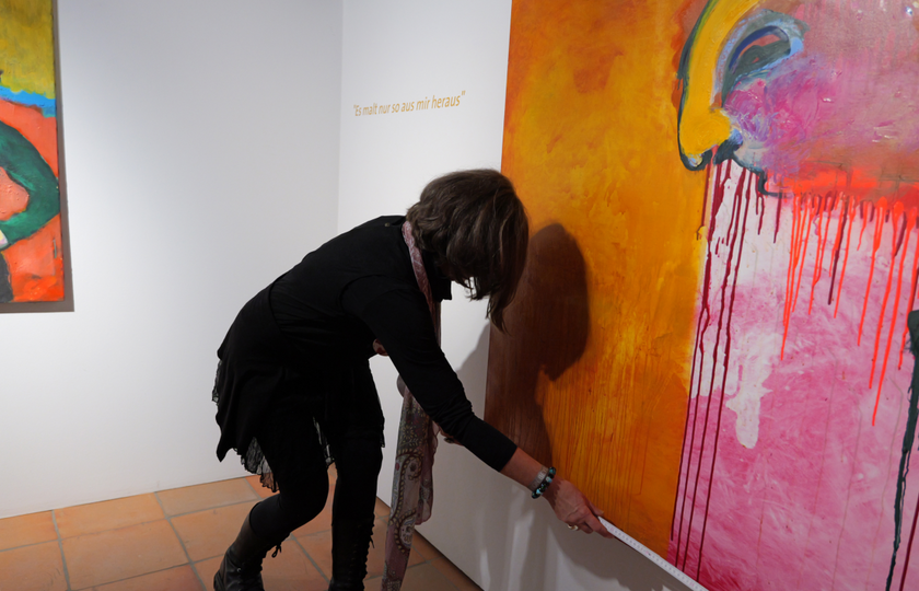 Oda Bauersachs steht vor dem Bild und misst seine Breite. Im Hintergrund das Zitat: "Es malt nur so aus mir heraus".