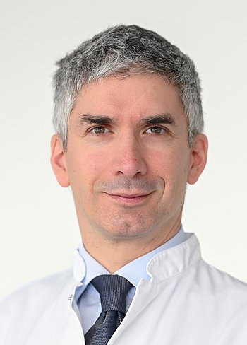 Portrait Peter Charbel Issa Portrait eines Mannes mit kurzem grauem Haar, weißem Hemd, weißem Kittel und blauer Krawatte