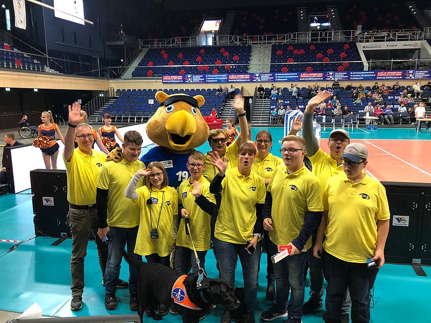 Eine Gruppe junger Menschen mit gelben Poloshirts mit PRO RETINA-Logo steht in einem Stadion. Im Hintegrund besetzte Zuschauerränge.