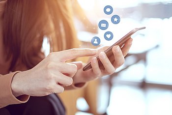 Eine Person bedient ein Smartphone, darüber sind Symbole für Nachrichten und soziale Kontakte eingeblendet.