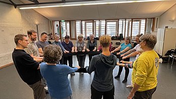 Teilnehmende des Selbstverteidigungskurses stehen in einem Kreis und halten gemeinsam ein Trainingsband. Alle sind konzentriert bei der Übung und haben sichtlich Freude am Mitmachen.