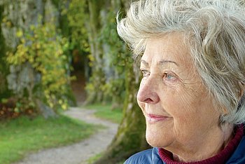 Eine Frau mit weißgrauem Haar schaut in die Ferne