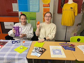 Zwei junge Frauen an einem Infostand mit Materialien und Sehhilfen zur „Woche des Sehens“.