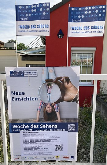 Plakat mit Werbung zur Woche des Sehens 2021, am oberen Ende sind zwei Fähnchen an das Plakat befestigt