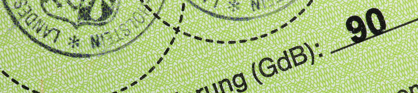 Ausschnitt eines grünen Ausweispapieres mit Stempeln auf dem der Grad der Behinderung abzulesen ist