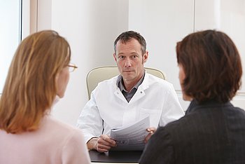 Ein Arzt hät mit zwei Frauen ein Patientengespräch ab.