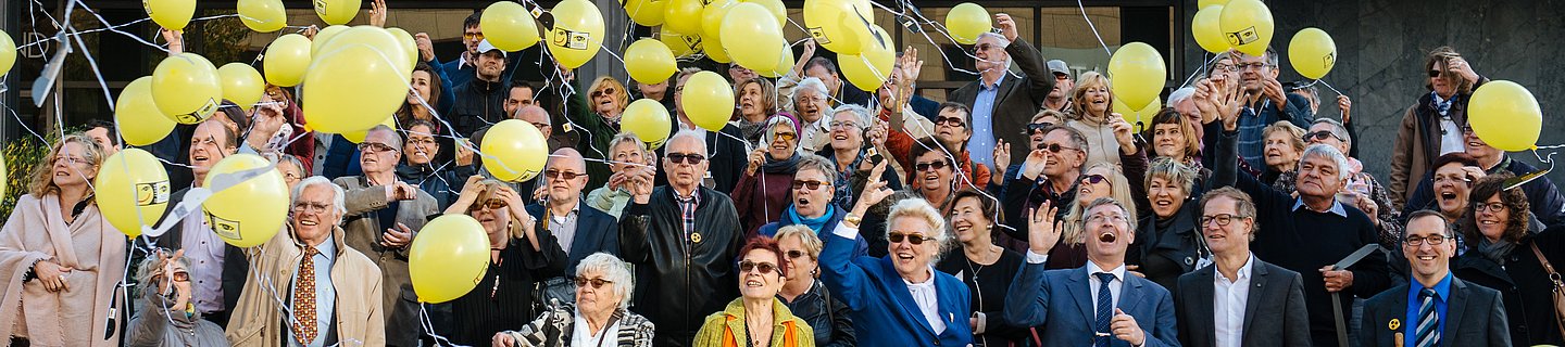 Viele Menschen stehen aufgereiht auf einer Treppe und lassen gelbe Luftballons steigen. 
