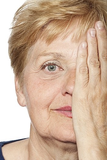 Eine Seniorin mit kurzen Haaren hält sich mit der Hand ein Auge zu